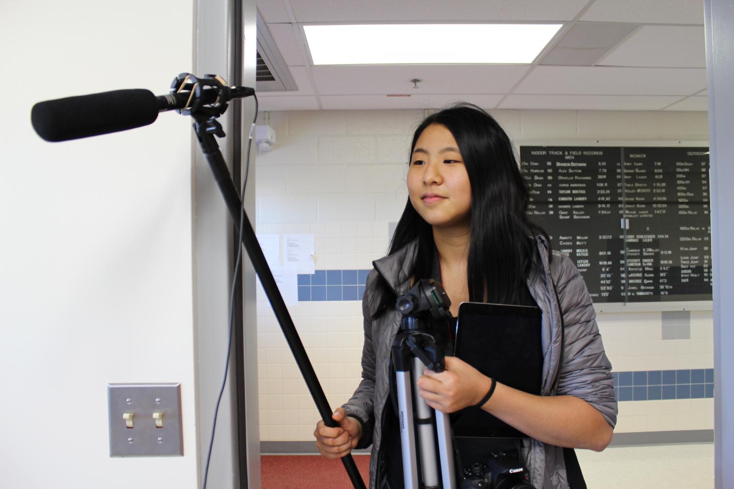 Carrying a <em>tjTV</em> tripod and microphone, Virginia Student Journalist of the Year Christine Zhao walks into the security room at Thomas Jefferson High School. Zhao was was preparing to interview security employee Charles Phillips for an online series on the stories of African-American students and staff.