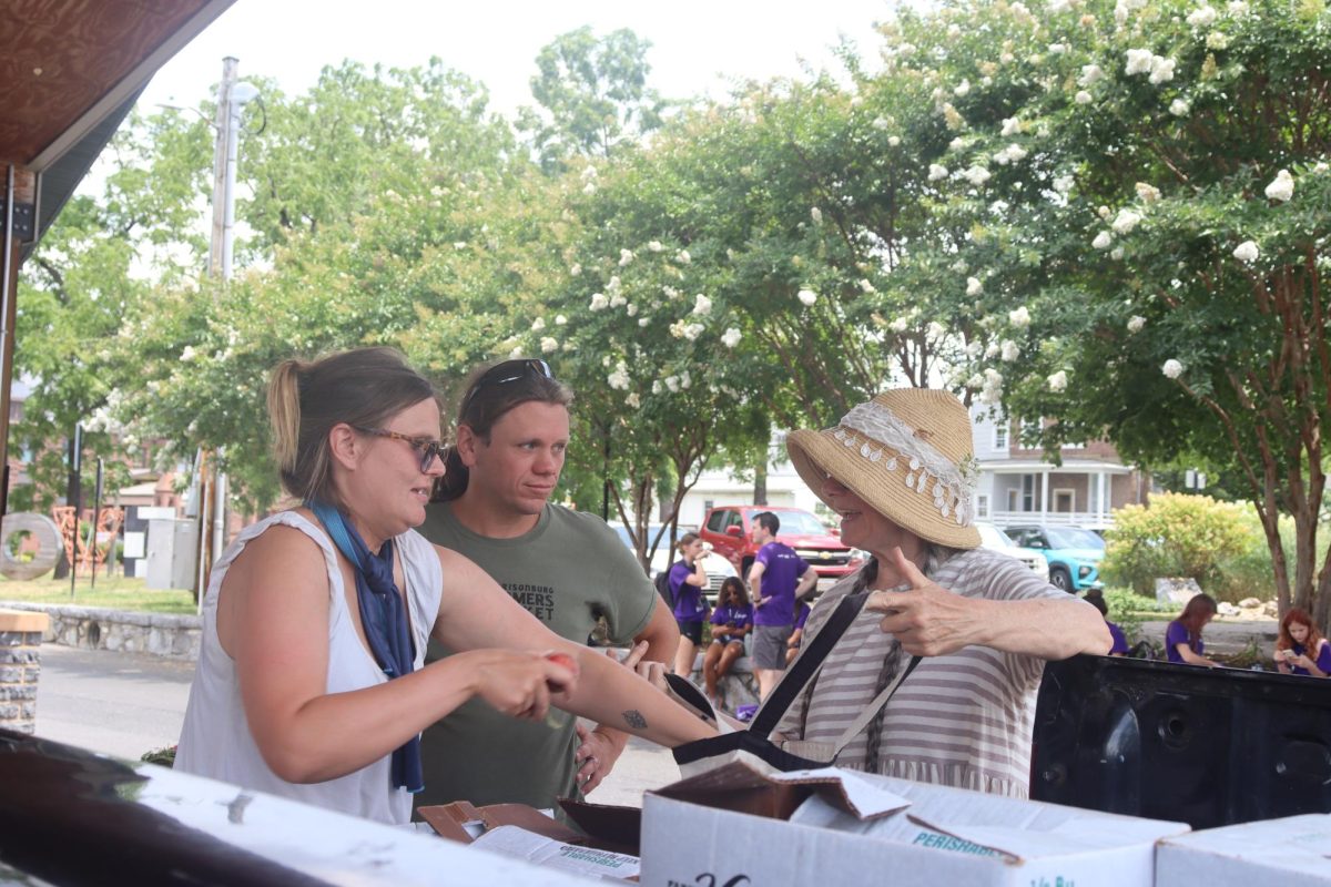 Patrick Ryan, middle, and Theresa Kubasak, right, stand at the Harrisonburg Farmers Market while Kubasak purchases fresh fruit July 9. Kubasak has been a frequent patron of the market for years after returning from her time in Damascus, Syria. “We moved here exactly eight years ago on July 31st on a Sunday. And when Tuesday came, I came to the Farmers Market. Those were the first friends I ever made in Harrisonburg,” Kubasak said.